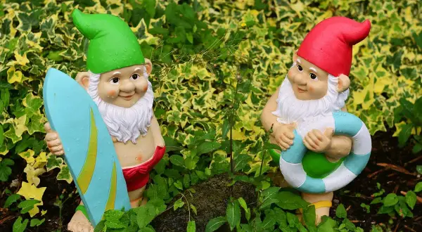 Dwa krasnale ogrodowe, jeden z deską surfingową, drugi z kołem ratunkowym. Idealne do ogrodu, czym pomalować krasnale ogrodowe?