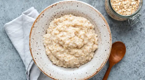 Cremiger Porridge im rustikalen Teller, daneben Haferflocken im Glas. Ein einfaches Porridge Rezept für einen guten Start.