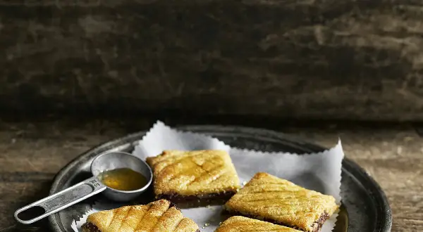 Quatre makrouts algériens sur une assiette, arrosés de miel. Une cuillère doseuse remplie de miel est à côté. Parfait pour une recette makrout algérien facile.