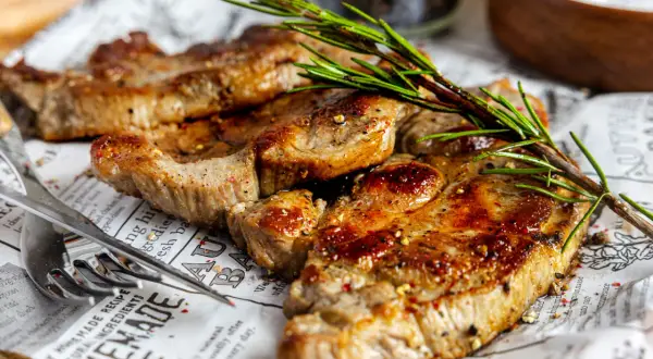 Saftiges Nackensteak im Backofen, perfekt gewürzt und mit Rosmarin garniert, liegt auf Zeitungspapier.