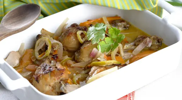 Muslitos de pollo guisados con verduras y limón, servidos en una cazuela blanca.