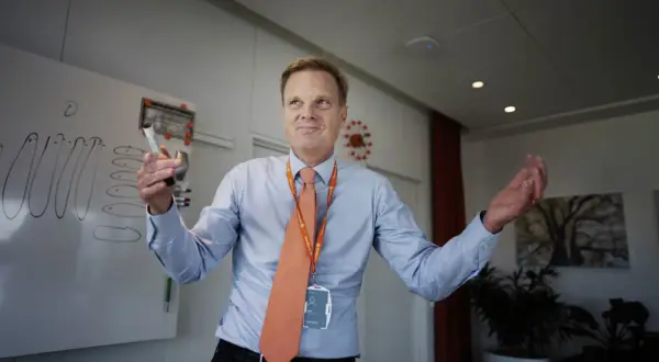 Swedbank vd med orange slips och namnskylt håller en penna vid en whiteboard.