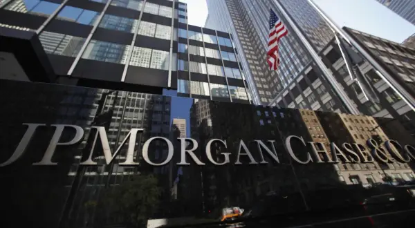 Błyszczący napis JP Morgan Chase & Co na tle drapaczy chmur i amerykańskiej flagi.