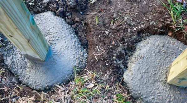 Holzpfosten werden in frischen Beton gesetzt. Die Tiefe, wie tief man einen Pfosten einbetonieren sollte, hängt von der Nutzung ab.