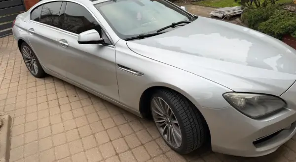 Srebrne BMW 640i z czarnym dachem stoi na podjeździe z kostki brukowej.