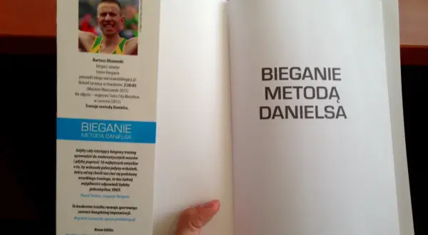 Otwarta książka z hasłem "Bieganie metodą Danielsa" na prawej stronie. Na lewej stronie zdjęcie biegacza i opis jego osiągnięć.