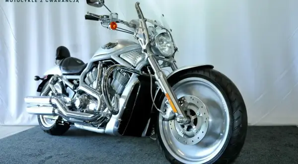 Srebrny motocykl typu cruiser z chromowanymi elementami, na tle białej ściany.
