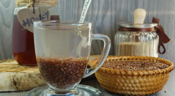 Szklanka z wodą i siemieniem lnianym, obok miód i koszyk z nasionami. Kiedy pić siemię lniane rano czy wieczorem? To pytanie o zdrowie.