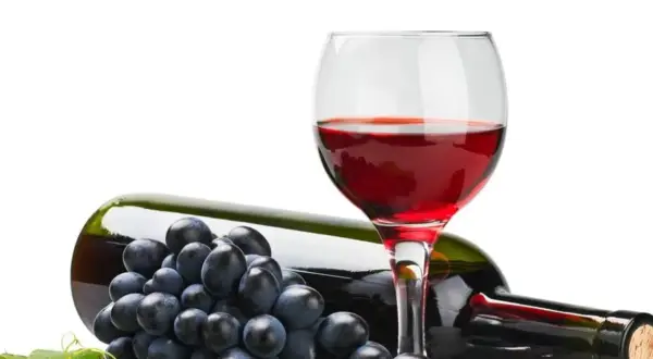Czerwone wino w kieliszku, butelka i winogrona. Czy wiesz, że resweratrol co to jest, znajduje się w skórce winogron?