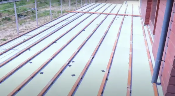 Drewniane legary ułożone na białej powierzchni, przygotowane do mocowania do betonu. Widać elementy mocujące.