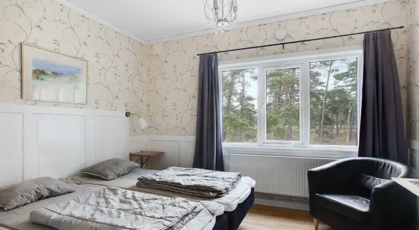 Mysigt rum på vandrarhem Gotland med två sängar, fåtölj och fönster med utsikt över skog.