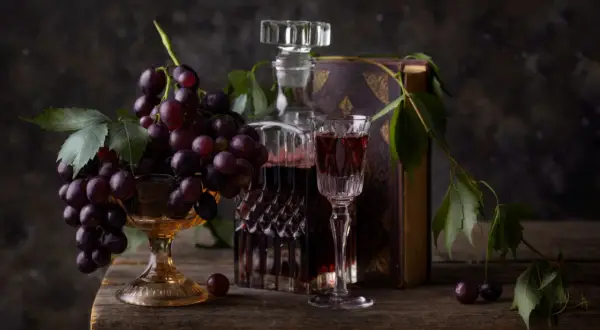 Kieliszek wina merlot veneto obok karafki i kiści winogron na drewnianym stole.