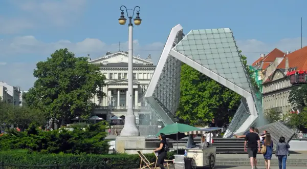 Plac Wolności tętni życiem. Ludzie spacerują obok nowoczesnej fontanny i lodziarni, ciesząc się słonecznym dniem.