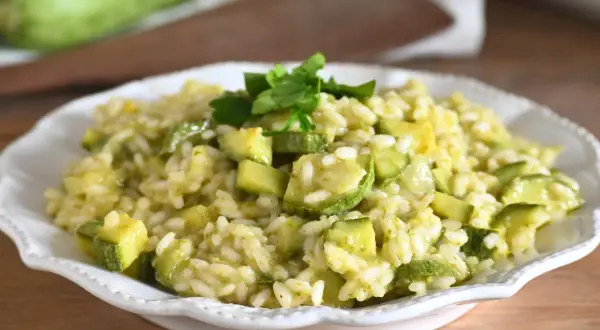 Un cremoso risotto con zucchine fresche, cotto in padella e guarnito con prezzemolo. Un piatto leggero e saporito.