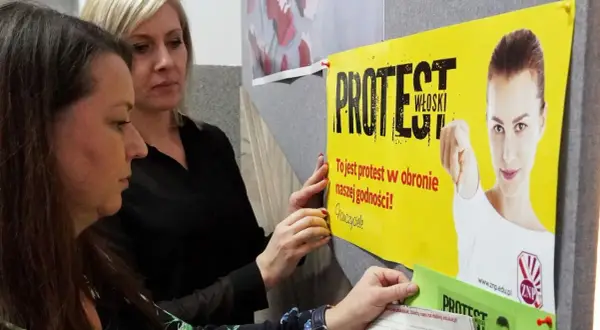 Dwie kobiety wieszają plakat "Protest Włoski" na tablicy. Hasło głosi: "To jest protest w obronie naszej godności!".