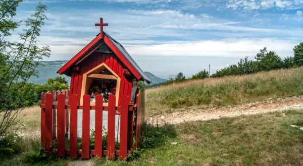Kapliczka na szlaku na Błatnią z Brennej. Czerwona, drewniana, z krzyżem i kwiatami.
