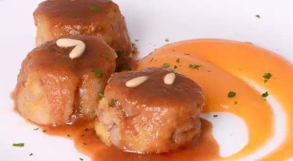 Deliciosas manitas de cerdo rellenas, bañadas en salsa y decoradas con piñones y perejil, acompañadas de puré de zanahoria.
