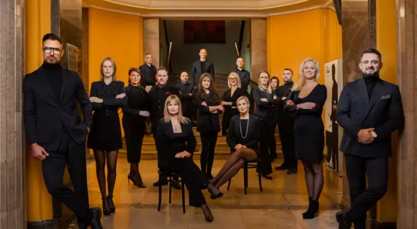 Grupa profesjonalistów w eleganckich strojach pozuje w holu.