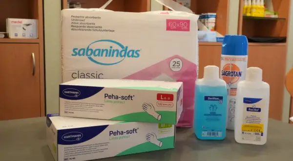 Pflegehilfsmittel Liste: Ein Paket Einlagen, zwei Schachteln Latex-Handschuhe, Desinfektionsmittel und ein Spray.
