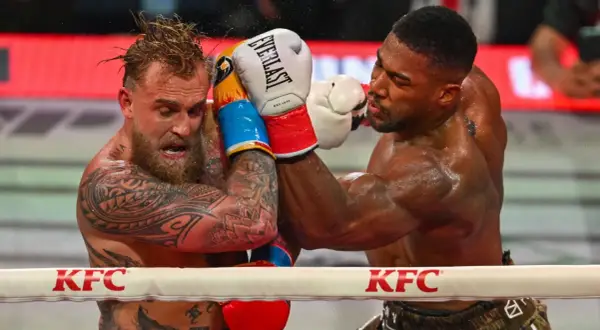 Two boxers grapple in the ring. One, with tattoos and wet hair, recoils from a punch. The other, muscular and focused, lands a blow. This is what heavyweight boxing looks like.