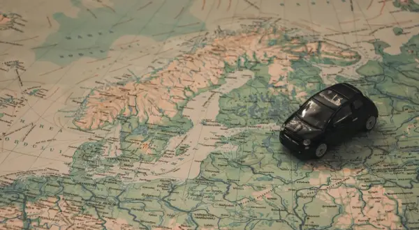 Czarny Fiat 500 na mapie Europy, sugerujący podróż do Włoch samochodem.