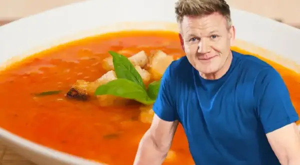 Gordon Ramsay obok talerza zupy pomidorowej z grzankami i bazylią.