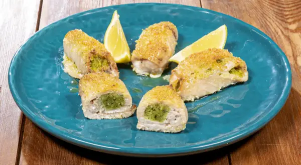 Involtini di pesce spada ripieni di erbe aromatiche, dorati e serviti su un piatto blu con spicchi di limone.