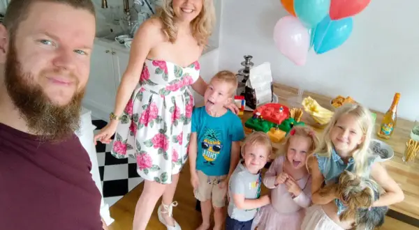 Rodzina świętuje roczek dziecka. Radosne dzieci, rodzice i piesek przy stole z tortem i balonami.