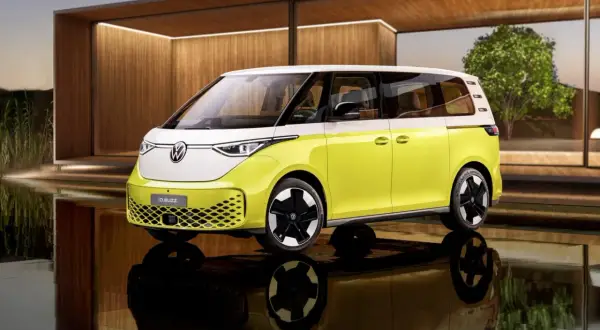 Nowy, elektryczny VW ID. Buzz w dwukolorowym malowaniu, z białym dachem i żółtym nadwoziem, stoi na tle nowoczesnej architektury.