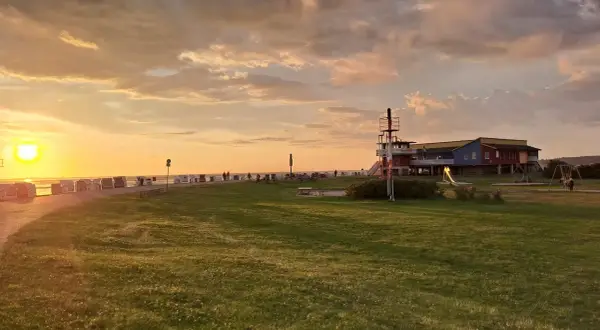 Sonnenuntergang am Husum Strand mit Strandkörben, einem Spielplatz und einem bunten Gebäude.