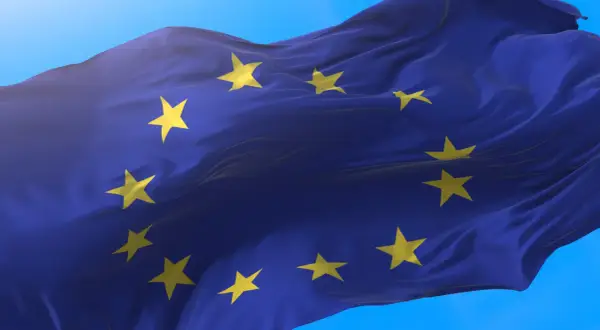 Flaga Unii Europejskiej falująca na wietrze na tle błękitnego nieba.