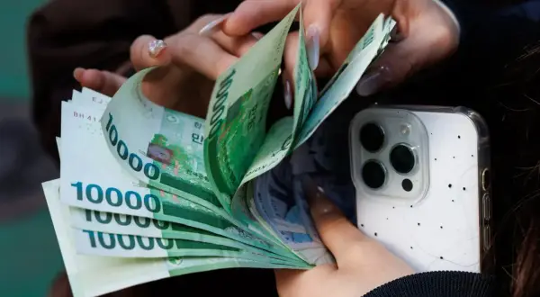 Dłonie liczą banknoty 10000 wonów, waluta Korei Południowej, obok białego etui na telefon.