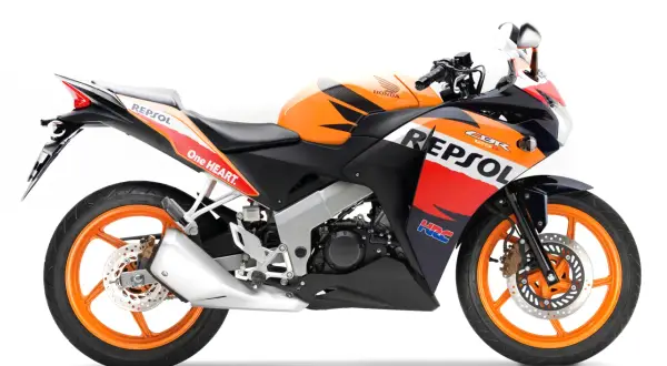 Pomarańczowo-czarny motocykl Honda CBR 125R w barwach Repsol, gotowy do jazdy z mocą V-max.