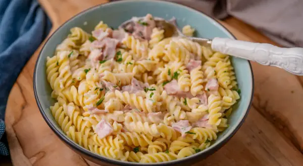 Fusilli-Nudeln in cremiger Schinken-Sahne-Sauce, garniert mit Petersilie. Ein köstliches Gericht, das zum Genießen einlädt.