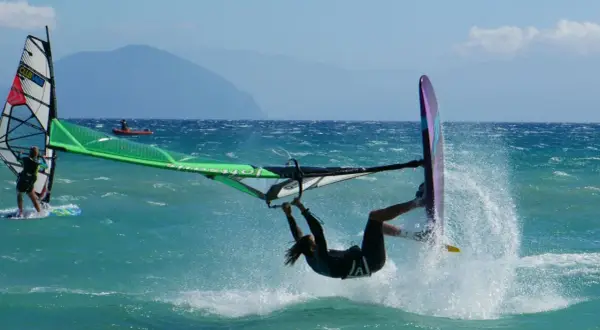 Windsurfer wykonuje akrobację na turkusowej wodzie, tworząc fontannę rozprysków.