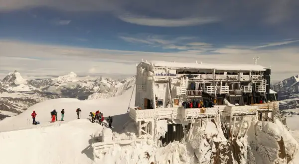 Die Capanna Margherita thront eisbedeckt auf einem Berggipfel. Bergsteiger genießen die Aussicht auf die verschneite Alpenlandschaft.