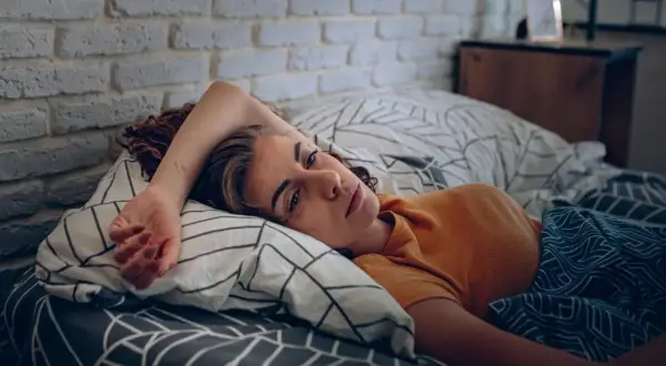 Eine Frau liegt im Bett, ihr Blick ist müde und nachdenklich. Sie kämpft mit den Symptomen eines Fatigue-Syndroms.