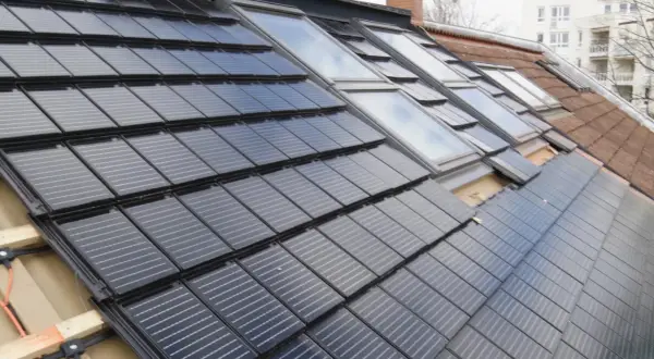 Dach renovieren kosten: Solarmodule werden auf einem Dach mit Dachfenstern installiert.