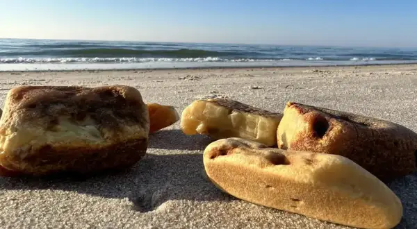 Kilka kawałków bursztynu leży na piaszczystej plaży, z morzem i błękitnym niebem w tle.