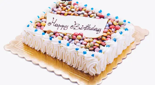Torta rettangolare con glassa bianca, decorata con tanti smarties colorati e la scritta "Happy Birthday".