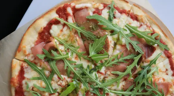 Pyszna pizza prosciutto z rukolą i sosem pesto.