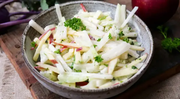 Kohlrabi Salat mit Apfelstücken und frischer Petersilie in einer rustikalen Schüssel.