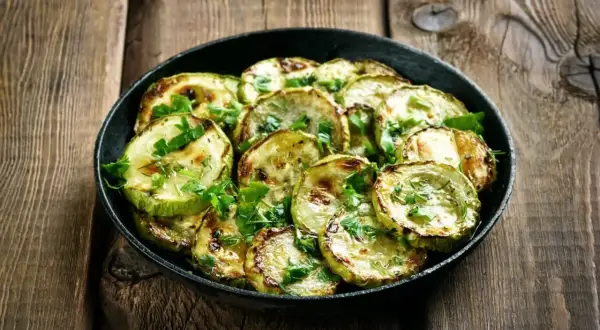 Zucchine marinate cotte, grigliate e guarnite con prezzemolo fresco, servite in una padella su un tavolo di legno rustico.