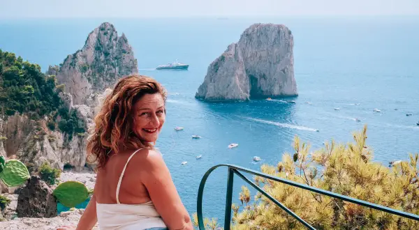 Donna sorridente con vista sui Faraglioni e il mare azzurro, un ricordo dalla spiaggia di Marina Piccola.