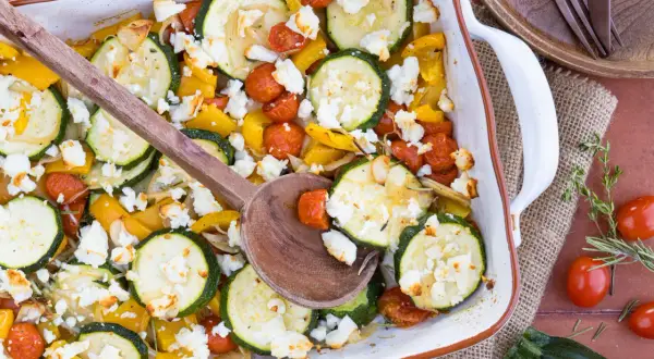 Gebackener Feta mit Zucchini, Kirschtomaten und gelber Paprika in einer Auflaufform, bereit zum Servieren.