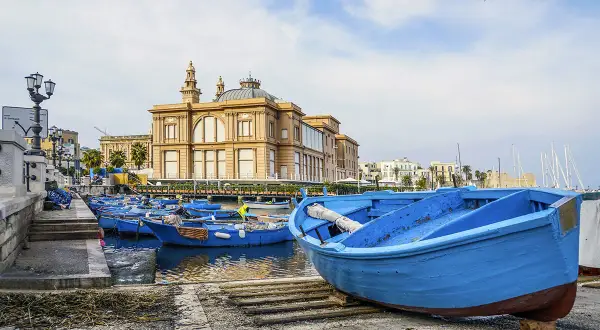 Barche blu nel porto del capoluogo della Puglia, con un edificio storico sullo sfondo.