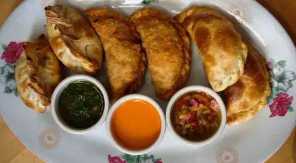 Empanadas de carne doradas y crujientes, servidas con tres salsas: chimichurri, picante y criolla.