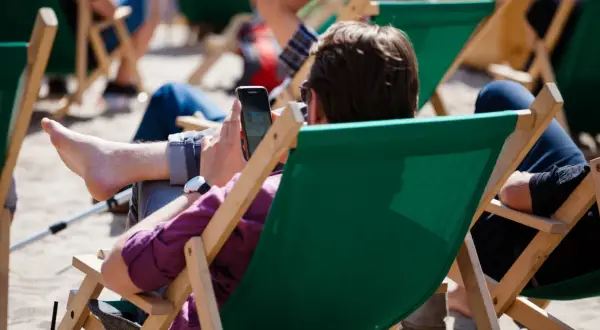 Mężczyzna w okularach przeciwsłonecznych relaksuje się na leżaku, przeglądając telefon. Idealny urlop wypoczynkowy.