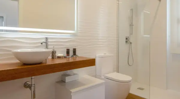 Baño moderno con lavabo sobre mueble de madera, inodoro y ducha con mampara de cristal. Perfecto para impermeabilizar ducha y mantener la limpieza.