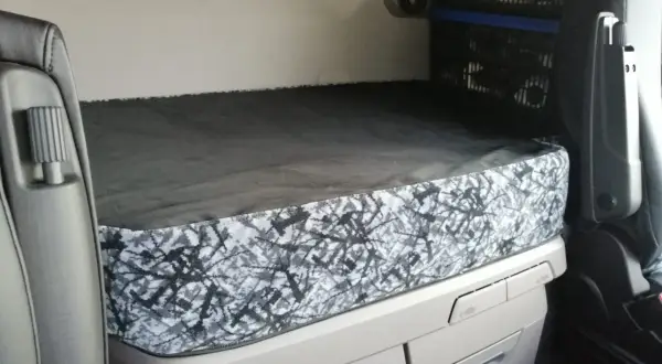 L'intérieur d'un camion Scania, prêt pour la nuit. Le lit est fait, avec une housse au motif abstrait gris et noir, parfait pour le scania tuning nuit.